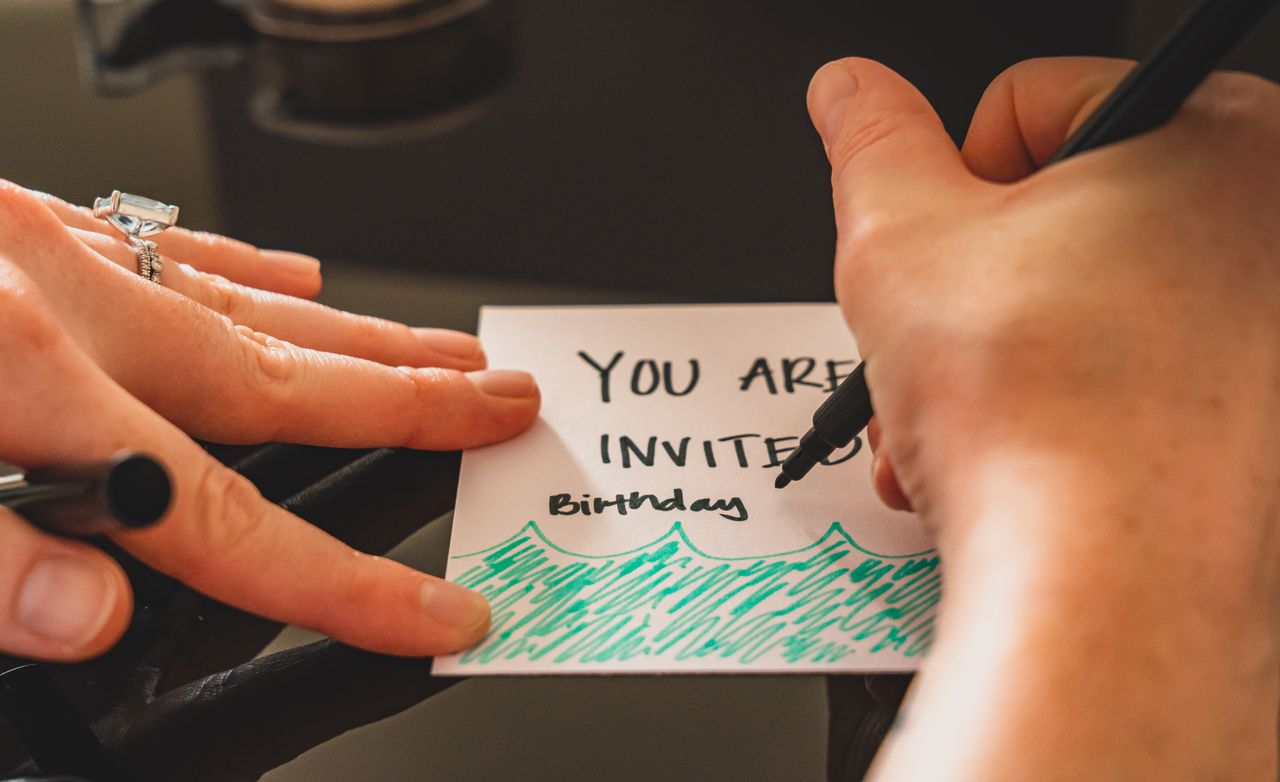 Crafting Captivating Headlines: Your awesome post title goes here Hands writing a personalized birthday invitation card using a marker on paper.